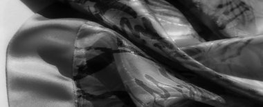 Soyut siyah fırça darbelerine sahip akışkan kumaşların yakın plan arkaplanı. Işık dokuyla hassas bir şekilde etkileşir..