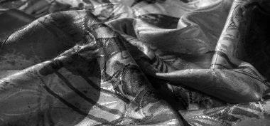 Soyut siyah mürekkep desenleri olan hassas bir kumaşın yakın çekimi. Yumuşak katlanmış, pürüzsüz dokusunu ve tek renkli detaylarını gözler önüne seriyor..