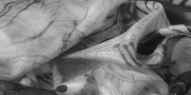 Yarı saydam, desenli bir yüzeye karşı soyut siyah fırça darbelerine sahip akışkan, dokulu bir kumaşın yakın çekimi.