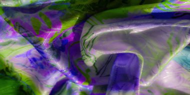 Soyut fırça darbeleri serpiştirilmiş mor ve yeşil kumaştan canlı bir görüntü. Parlak yüzey ışığı yakalar, yumuşak kumaşlarla akışkan ve dinamik bir görüntü oluşturur..