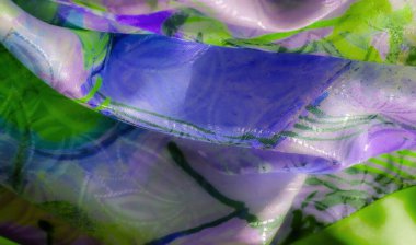 Yumuşak kıvrımlı mor ve yeşil kumaşların renkli bir görüntüsü, parlak vurgular parlak dokuyu ve soyut desenleri yansıtıyor.