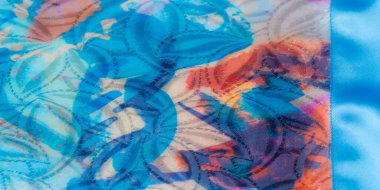 Parlak kaplamalı kıvrımlı renkli kumaşın yakın plan görüntüsü, mavi, mor ve pembe tonlarında soyut desenler sergiliyor..