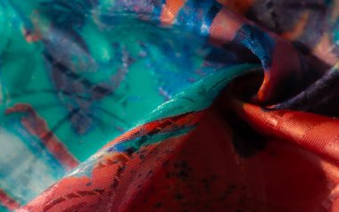 Mavi, pembe ve sarı tonlarında soyut desenler içeren renkli, parlak bir kumaş girdabı yumuşak, lüks bir doku yaratıyor.