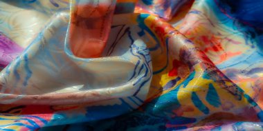 Sarı, mavi ve pembe renkli parlak suluboya desenli soyut kumaşların yakın çekimi yumuşak kıvrımlar halinde kıvrılarak pürüzsüz ve parlak bir dokuyu gösteriyor..