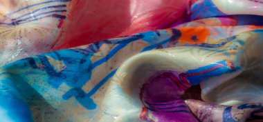 Mavi, sarı ve pembe gibi canlı renklere sahip çok renkli, soyut bir kumaşın yakın çekimi. Doku ve akış dinamik, yumuşak ve parlak bir görünüm yaratır..