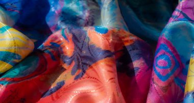 Sarı, kırmızı, mavi ve mor tonlarında koyu renk lekeleri olan parlak, canlı, soyut kumaş. Yumuşak parıltı ve karmaşık tekstil kıvrımları dinamik bir sanatsal görünüş yaratır..