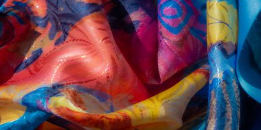 Mavi, sarı, kırmızı ve yeşil desenli soyut kumaş karışımı. Kumaşın pürüzsüz yüzeyi ışığı yansıtır, dokusunu ve renk eğimini vurgular..