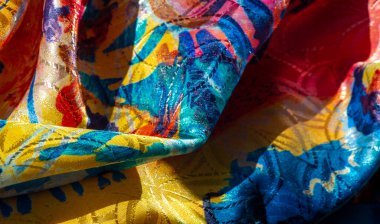 Mavi, pembe ve sarı lekeli parlak, soyut bir tekstil manzarası. Parlak bitiş, kumaşın zengin dokularını ve kıvrımlarını vurgular.