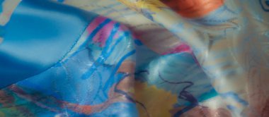 Kıvrımlı mavi, pembe ve sarı desenli canlı kumaş, parlak yüzeyindeki ışığın etkileşimini yakalıyor.