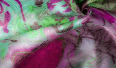 Soyut desenleri ve yumuşak kıvrımları olan pembe ve yeşil bir kumaş yakın plan, zengin bir görsel doku ve canlı bir kontrast yaratır..