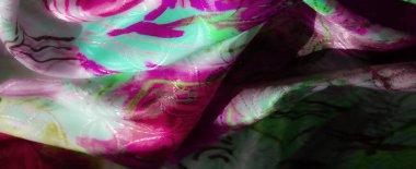 Derin pembe ve parlak yeşil tonlarda, soyut desenleri ve ışığı yakalayan pürüzsüz, yansıtıcı bir yüzeyi olan bir kumaşın yakın çekimi..