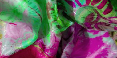 Parlak, yeşil ve pembe soyut tekstil yüzeyden yansıyan ışıkla yakın plan, maddenin karmaşık detaylarını vurguluyor.