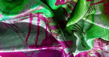 Yumuşak kıvrımlı parlak yeşil ve morumsu kumaş, soyut desenler ve parıldayan doku. Işık yüzeyde yankılanır, lüks ve dinamik özelliklerini vurgular.