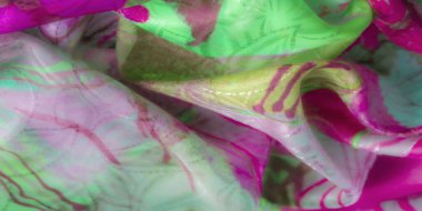 Karmaşık tasarım desenleri olan yeşil ve pembe örtülü kumaşın dokuyu ve yansıtıcı unsurları gösteren yakın çekimi.