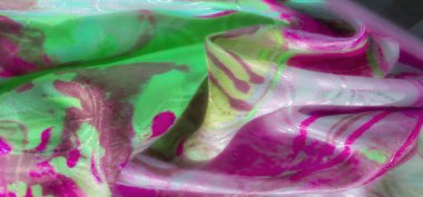 Karmaşık tasarım desenleri olan yeşil ve pembe örtülü kumaşın dokuyu ve yansıtıcı unsurları gösteren yakın çekimi.