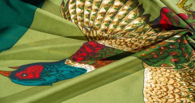 Yeşil zemin üzerinde uçan bir sülünün canlı bir çizimi. Karmaşık tüy detayları ve koyu kırmızı, yeşil ve mavi renkler..