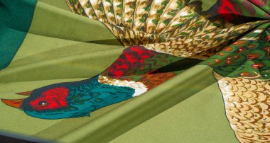 İpeksi yeşil kumaş üzerinde ayrıntılı tüyleri olan iki sülünün sanatsal tasviri, zengin renkler ve karmaşık tasarım modelleri sergiliyor..