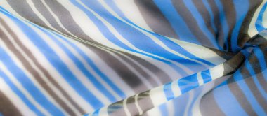 Kumaş kıvrımlarla örtülmüş. Mavi, beyaz ve kahverengi çizgiler akıcılık ve hareket hissi ekler..