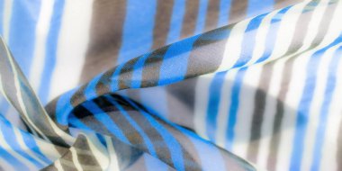 Mavi, beyaz ve açık kahverengi tonlarında dikey çizgileri olan, yumuşak ve pürüzsüz bir dokuyu gösteren hafif bir kumaşın yakın çekimi..