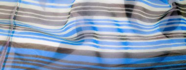 Yatay mavi, kahverengi ve beyaz çizgileri olan şeffaf bir kumaş, pürüzsüz kıvrımlarını ve dalgalı dokusunu yakalıyor..