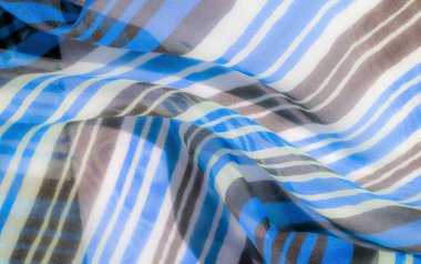 Yatay mavi, kahverengi ve beyaz çizgileri olan şeffaf bir kumaş, pürüzsüz kıvrımlarını ve dalgalı dokusunu yakalıyor..