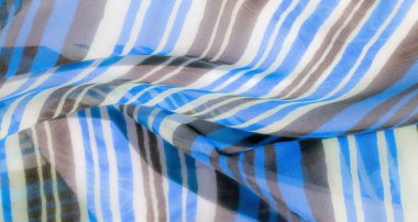 Pürüzsüz kumaş üzerinde mavi, beyaz ve gri dikey çizgiler, karmaşık katlar ve perdeler, tekstile dinamik ve dokulu bir görünüm verir..