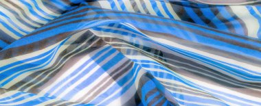 Dalgalı desenli, değişken mavi, kahverengi ve beyaz çizgili yumuşak, havadar bir kumaş, hafif ve zarif bir görsel efekt yaratır..