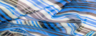 Yumuşak, dalgalı mavi, kahverengi ve beyaz çizgili şeffaf kumaş, zarif kıvrımlı pürüzsüz, akıcı bir doku sergiliyor..