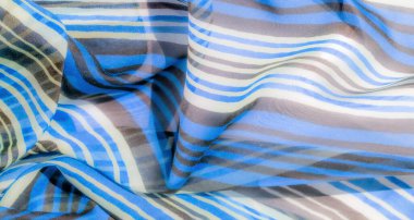 Yatay mavi, kahverengi ve beyaz çizgileri olan şeffaf bir kumaş, pürüzsüz kıvrımlarını ve dalgalı dokusunu yakalıyor..