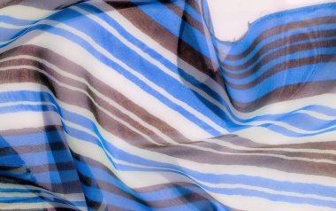 Yumuşak, dalgalı mavi, kahverengi ve beyaz çizgili şeffaf kumaş, zarif kıvrımlı pürüzsüz, akıcı bir doku sergiliyor..