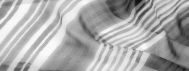 Gri tonlarda köşegen çizgileri akan bir kumaşın tek renkli yakın çekimi. Kumaşın yarı şeffaf, hassas bir kalitesi var. Hareket ettikçe dinamik ve yumuşak kıvrımlar oluşturuyor..