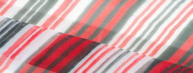 Kırmızı, beyaz ve yeşil çizgili kumaşların soyut yakın çekimi yumuşak kıvrımları ve karmaşık dokuyu yakalıyor. Parlak çizgiler uyum içinde harmanlanarak, materyalde akış ve hareket hissi verir.