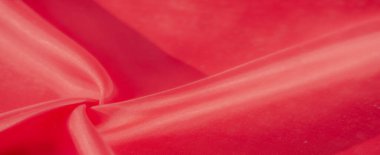 Zarif kıvrımlarda düz kırmızı kumaşın yakın plan görüntüsü, zengin dokuyu ve ışığın etkileşimini yakalıyor. Karmaşık dokuma ve yumuşak parıltı tekstilin lüks kalitesini vurguluyor..