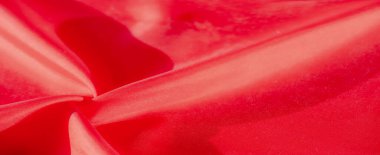 Zarif kıvrımlarla katlanmış pürüzsüz ve ipeksi bir dokusu olan kırmızı bir kumaşın yakın çekimi. Maddenin yüzeyi ışığı yakalar, örgünün ince desenlerini ve akan doğayı vurgular.