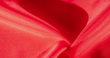 Zarif kıvrımlarla katlanmış pürüzsüz ve ipeksi bir dokusu olan kırmızı bir kumaşın yakın çekimi. Maddenin yüzeyi ışığı yakalar, örgünün ince desenlerini ve akan doğayı vurgular.