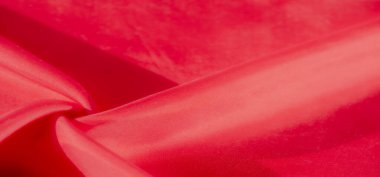Zarif dokumasını ve canlı rengini gösteren kırmızı bir kumaşın çarpıcı yakın çekimi. Kumaş nazikçe katlanır, hem yumuşaklık hem de sıcaklığı çağrıştıran zengin, dokunsal bir doku sunar..