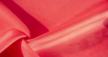 Kırmızı kumaşın detaylı bir yakın çekimi pürüzsüz kıvrımları ve kıvrımları olan zengin bir dokuyu ortaya çıkarıyor. Canlı kırmızı renk yumuşak, lüks yüzeyini vurgular, sıcaklık ve zarafet hissi yaratır..