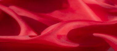 Yumuşak ve akışkan kıvrımlarla güzelce örtülmüş kırmızı kumaşın yakın çekim görüntüsü. Karmaşık dokuma ve ışık yansıması materyalin zarif ve hassas doğasını vurgular..