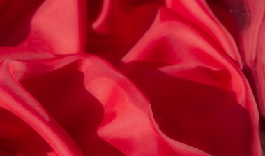 Yumuşak kıvrımlı canlı kırmızı bir kumaş, narin dokusunu gösteriyor. Yumuşak madde, güzel ışık yansımalarıyla pürüzsüz bir yüzey yaratır. Zengin ve lüks kalitesini yakalar..