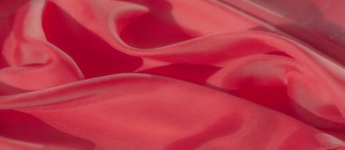 Dalgaları andıran kırmızı kumaşların detaylı bir yakın çekimi. Doğa örtüsü ve ışık yansıması tekstile bir hareket ve akıcılık hissi katarak pürüzsüz ve parlak dokusunu vurguluyor..