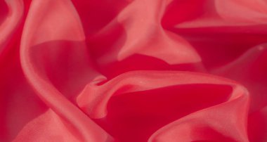 Dalgaları andıran kırmızı kumaşların detaylı bir yakın çekimi. Doğa örtüsü ve ışık yansıması tekstile bir hareket ve akıcılık hissi katarak pürüzsüz ve parlak dokusunu vurguluyor..