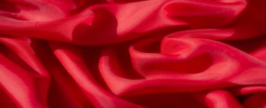 Lüks kırmızı bir kumaş, yakın plan çekilmiş, yumuşak, akışkan kıvrımlarını ve hassas kıvrımlarını gösteriyor. Materyalin dokusu ve ayrıntısı ışık oyunuyla geliştirilir.