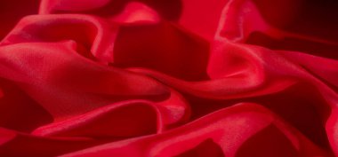 Lüks kırmızı bir kumaş, yakın plan çekilmiş, yumuşak, akışkan kıvrımlarını ve hassas kıvrımlarını gösteriyor. Materyalin dokusu ve ayrıntısı ışık oyunuyla geliştirilir.