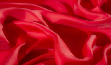 Pürüzsüz, dalgalı kırmızı kumaştan oluşan bir makro çekim. Parlak dokusunu ve yansıtıcı yüzeyini vurguluyor. Kumaşlar yumuşak, ipeksi kıvrımlar vurgulanmış doku desenleriyle dinamik ve zarif bir görüntü oluşturur..