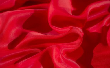 Dinamik kıvrımları ve yumuşak akışkan dokusu olan kırmızı kumaşın canlı bir görüntüsü ışık ve gölgenin etkileşimi soyut bir görsel etki yaratan maddenin derinliğini ve ipeksi görünümünü vurgular.