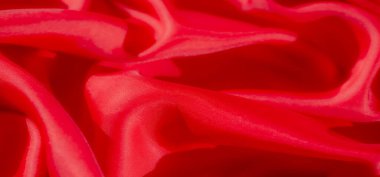 Pürüzsüz, dalgalı kırmızı kumaştan oluşan bir makro çekim. Parlak dokusunu ve yansıtıcı yüzeyini vurguluyor. Kumaşlar yumuşak, ipeksi kıvrımlar vurgulanmış doku desenleriyle dinamik ve zarif bir görüntü oluşturur..