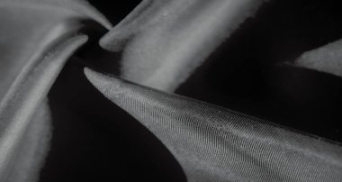 Siyah ve gri tonlarında, ince kıvrımlar ve kıvrımlarla yakalanmış açık renk kumaşın karmaşık hareketi. Yüzey ışığın etkileşimini gösterir, kumaşa parlak bir parıltı verir..