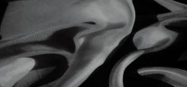 Yumuşak, dalgalı kumaşlardan oluşan, yumuşak kıvrımlı, karmaşık gölgeler ve röfleler yaratan bir yakın plan. Doku, materyalin narin parıltısını ve akışkan doğasını yakalar. Huzurlu bir görsel sunar..