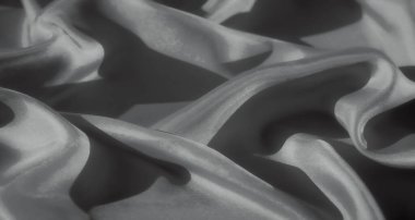 Karmaşık bir kumaş, yumuşak dokusunu vurgulayarak karamsar bir ışıkla çekilir. Işığın ince oyunu derinlik katar, hassas kırışıklıkları ve maddenin akışını vurgular..