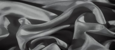 Örtülü kumaşın yakın plan bir görüntüsü, pürüzsüz ve yumuşak bir şekilde gri tonda renklendiriliyor. Gölgelerin hassas dokusu ve oyunu kumaşın akıcılığını ve yumuşaklığını vurgular.,